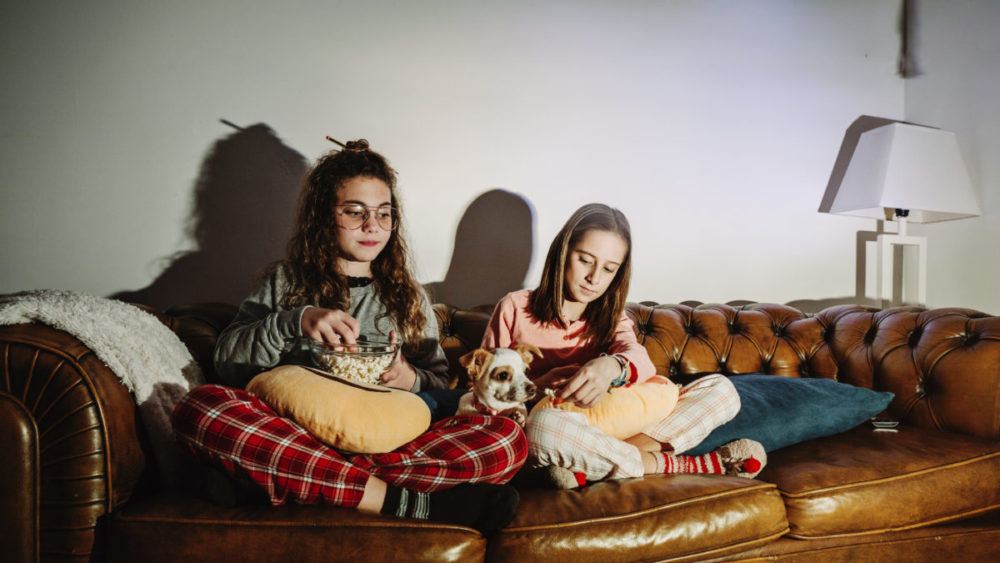Dicas para cuidar do cachorro no carnaval 2 Duas garotas assistindo tv com seu cachorro ao meio