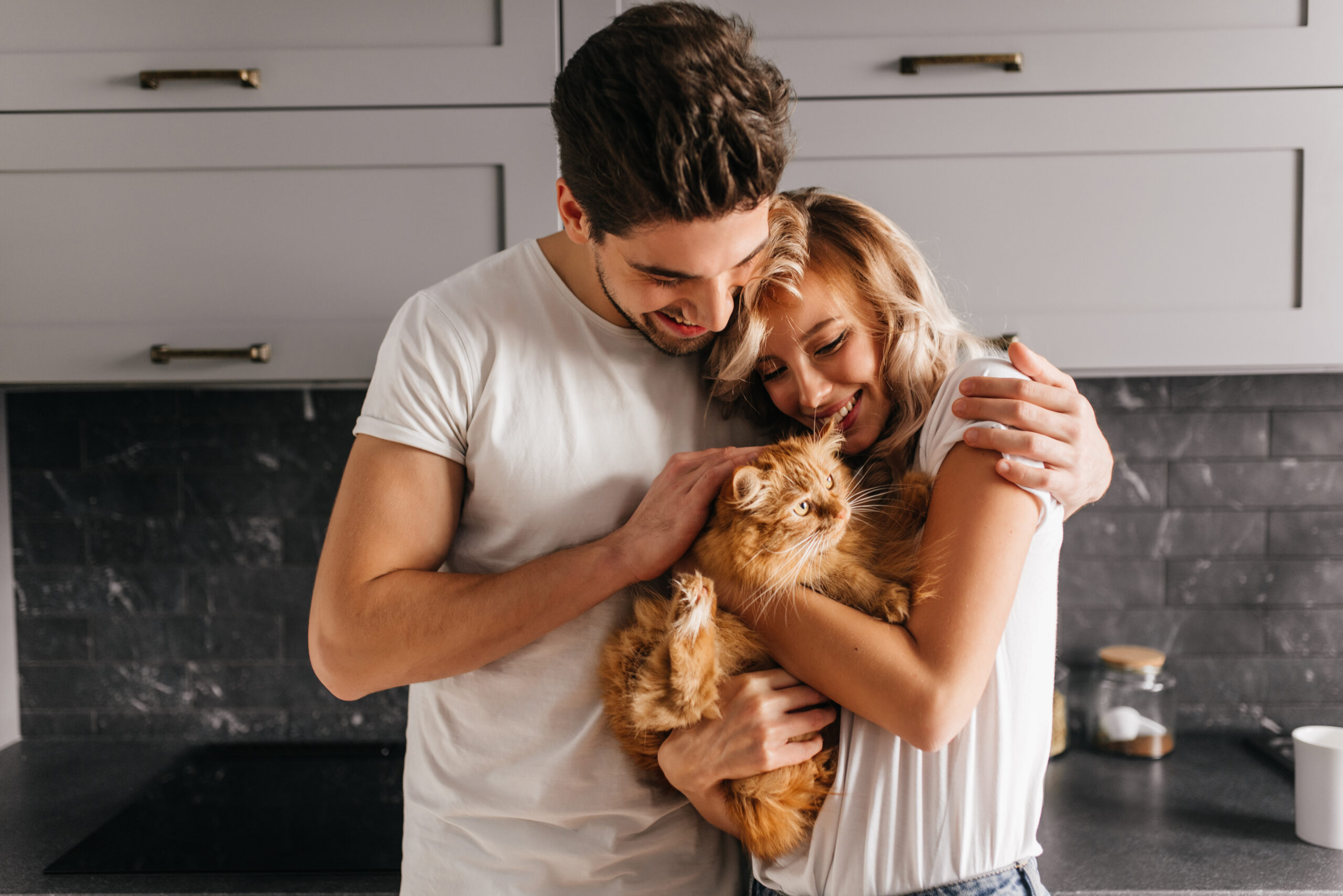 8 dicas para cachorros saudáveis 2 Brunette man looking at his cat and embracing wife. Indoor photo of happy family posing with pet.